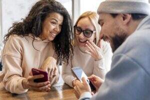 mulher sorrindo com celular na mão, mulher sorrindo com mão próxima a boca e homem sorrindo com celular na mão, com o programa indique e ganhe da vendizap